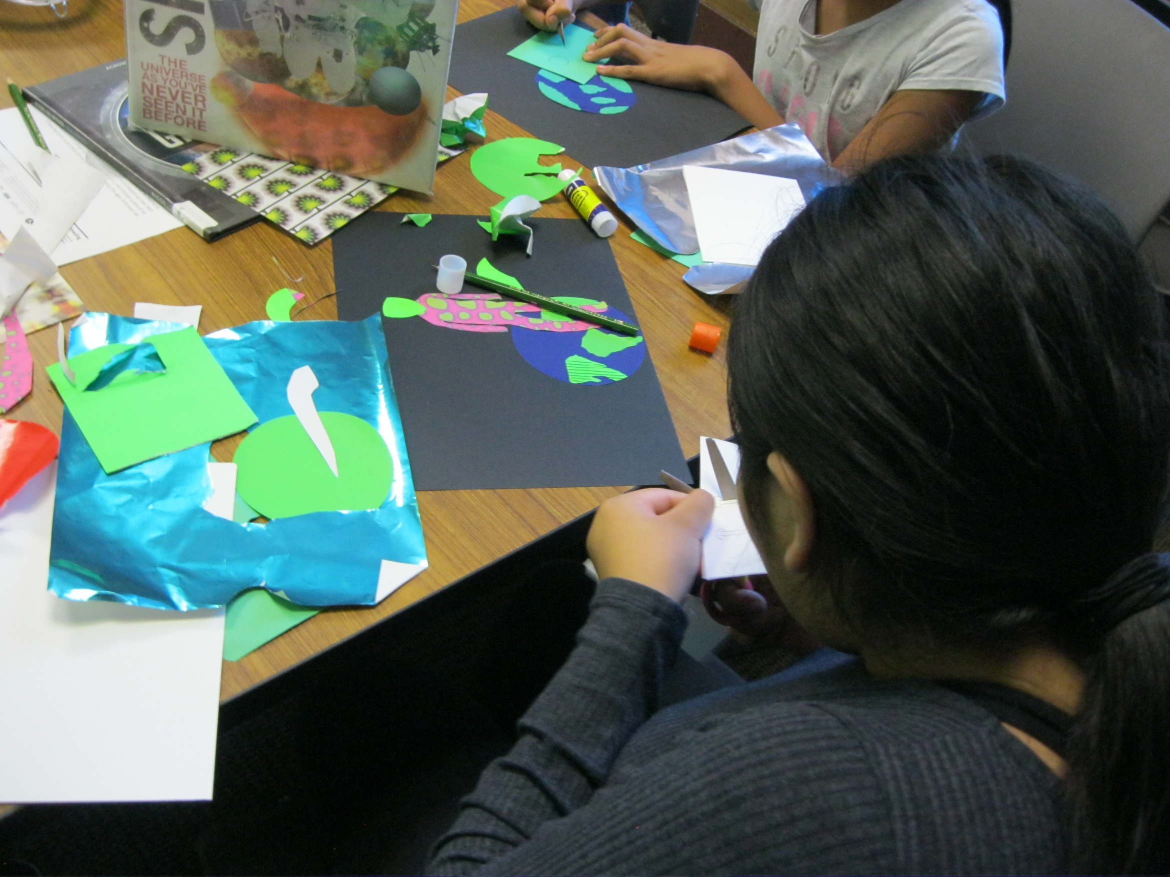 A workshop participant concentrates on cutting, while her alien collage waits for her next move. 