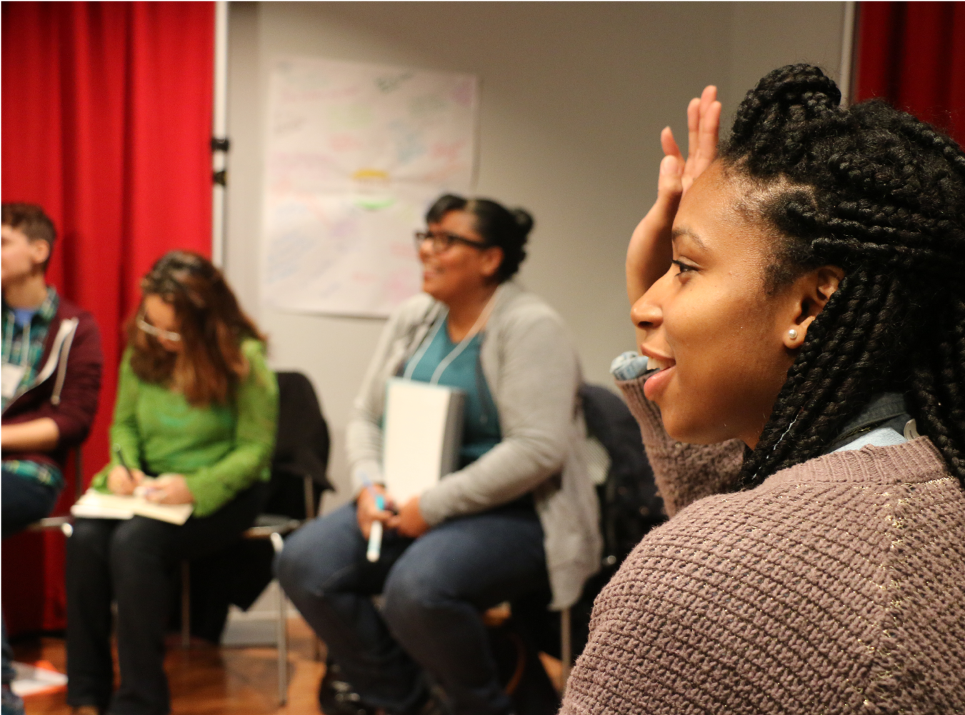 Teaching Artist Project participant in profile raises her hand for recognition in classroom.