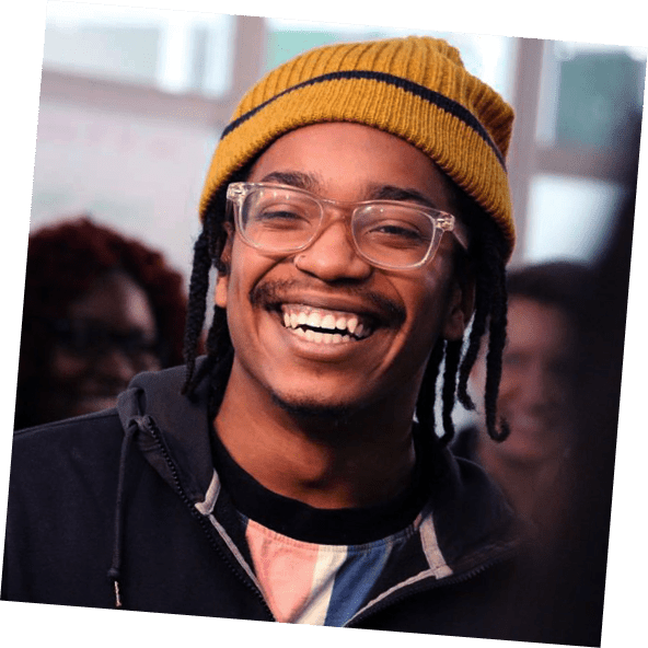 Young smiling man with ochre hknitted hat and transparent glasses frames.