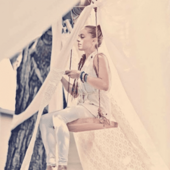 Woman women sitting on a swing hanging from tree branch inside hanging white fabric