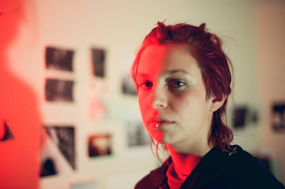 Portrait of woman in a studio with images on the wall in the background and half her face with bright red light