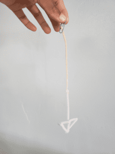 hand at top of frame hold the end of a pipe cleaners arrow pointing downward