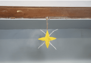 Small yellow paper start sculpture hanging from a wooden beam