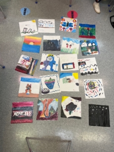 Student painting from above gathered together on the floor as a Quilt of Kindness