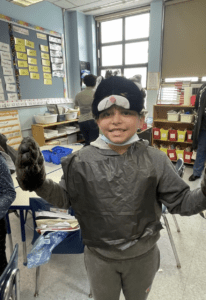 Second grade student dressing in disguise with large cartoon style holloween mask of a happy rat