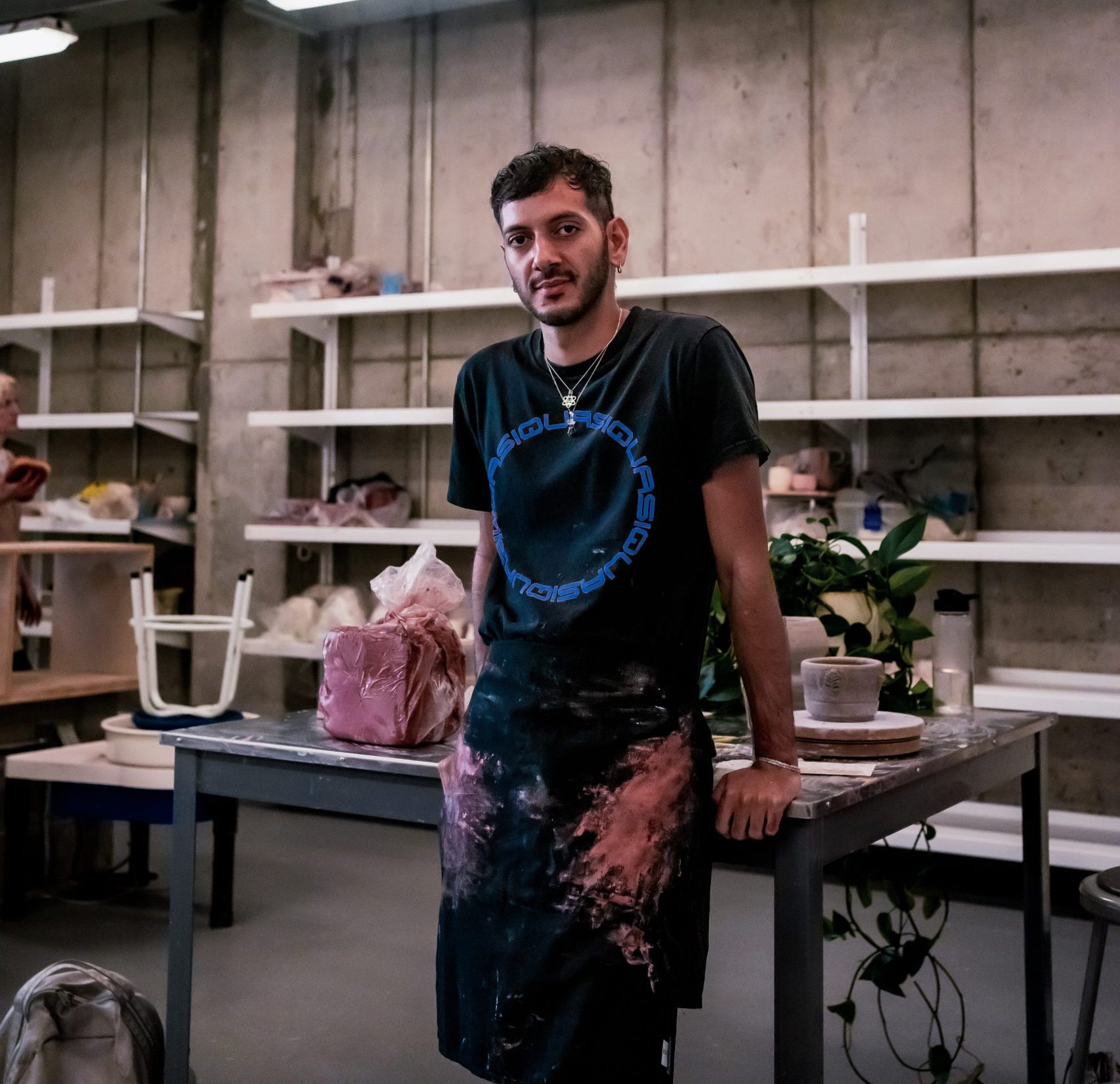 A photo of Jordany in an art studio leaning on a table