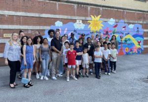Group of youth artists at Boys and Girls Club of Queens in front of a colorful wall mural about clean energy and protecting the planet