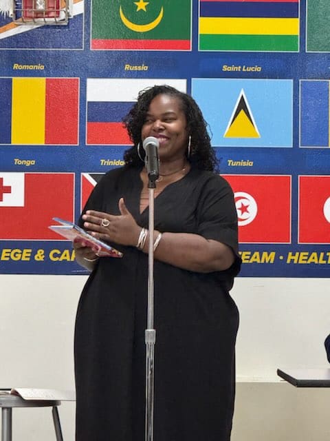 Woman at microphone reading from a book of poetry to young women