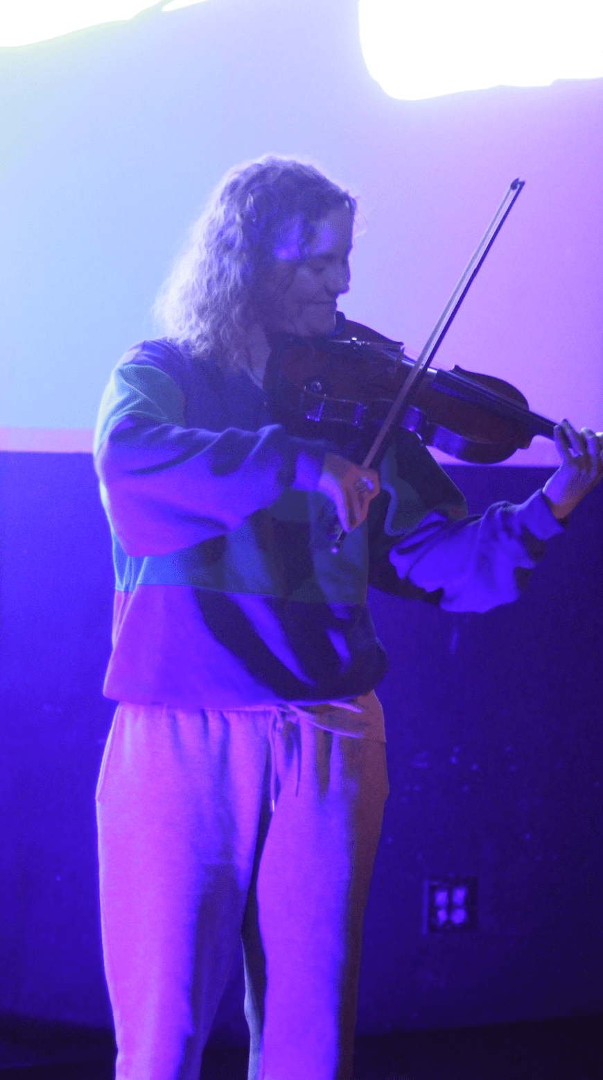 Woman plays violin standing in a dark room with deep purple and pink lights