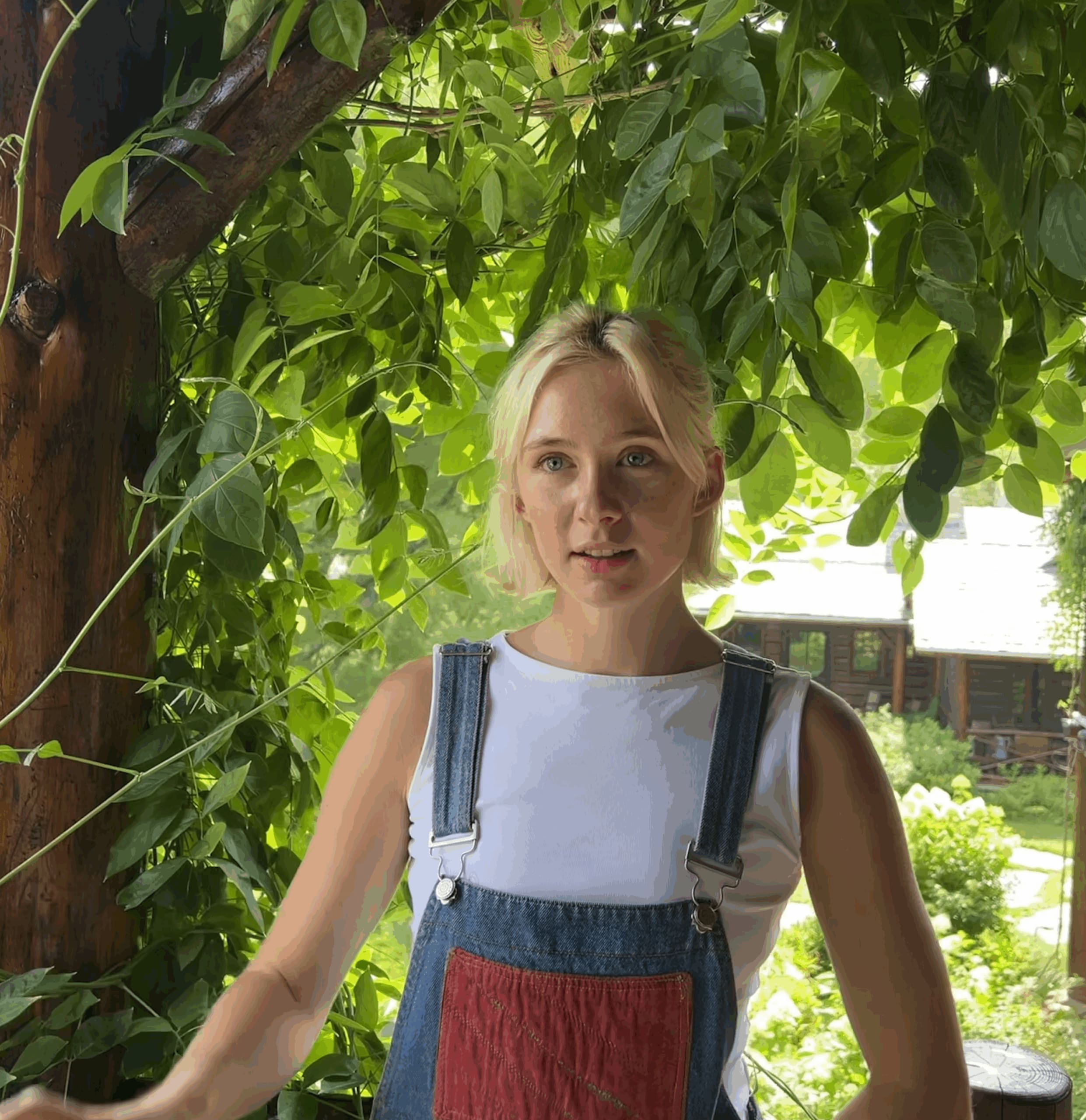 Woman in overalls in front of trees looking at camera