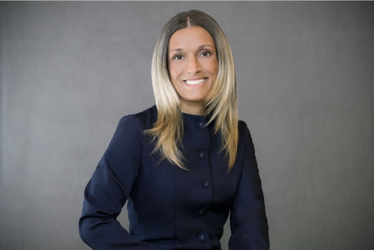 Woman smiling into camera in front of plain background