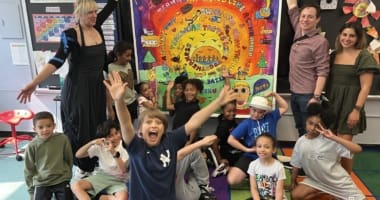 Young students in a classroom pulling faces with their teachers holding up there painting behind them