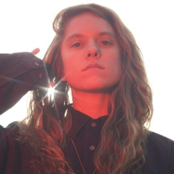 Portrait of a person dressed in black from below with sun behind her and an orange-red light on her face