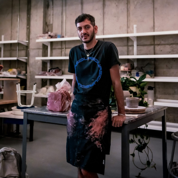 A photo of Jordany in an art studio leaning on a table