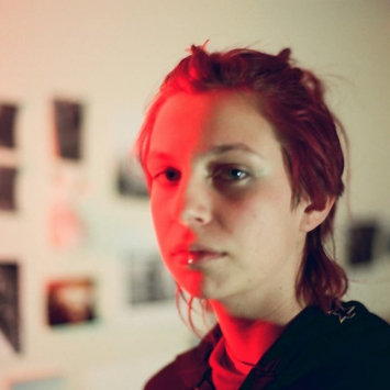 Portrait of woman in a studio with images on the wall in the background and half her face with bright red light