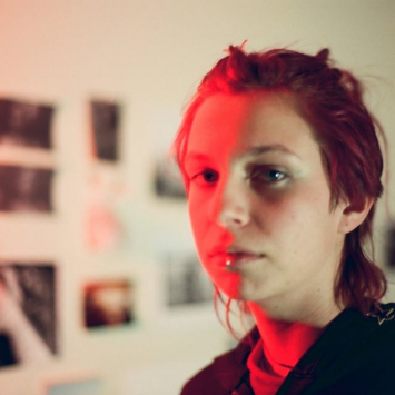 Portrait of woman in a studio with images on the wall in the background and half her face with bright red light