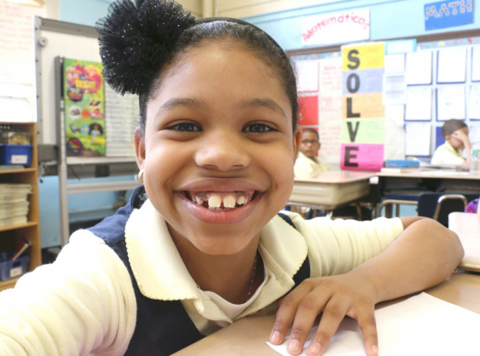 Middle school female student in classroom wearing uniform and smiling broadly