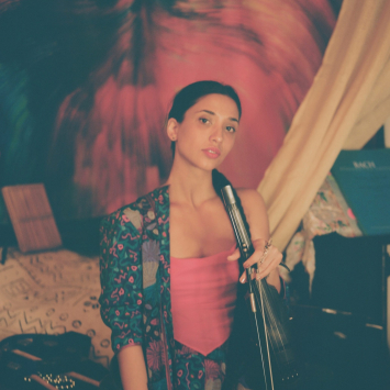 A photo of Natie standing in front of a mic with a multicolored backdrop behind her.