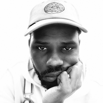 Black and white portrait of a man in a baseball cap resting his chin on his hand.